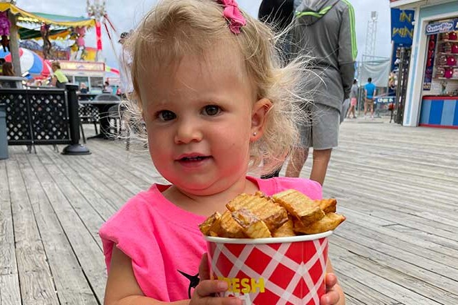 Little girl holding a cup of Curley's Fries on the boardwalk