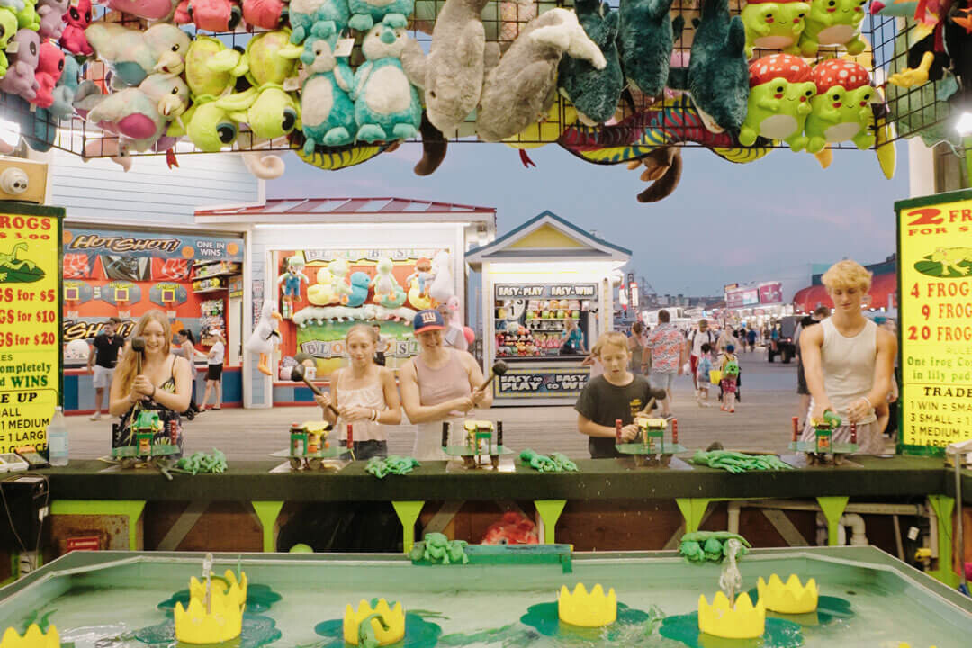 Players at a boardwalk water race game with plush prizes overhead